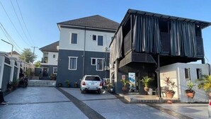 A residential street with a two-story house, a parked car, and potted plants. - Deroche Apartment (Abuja)