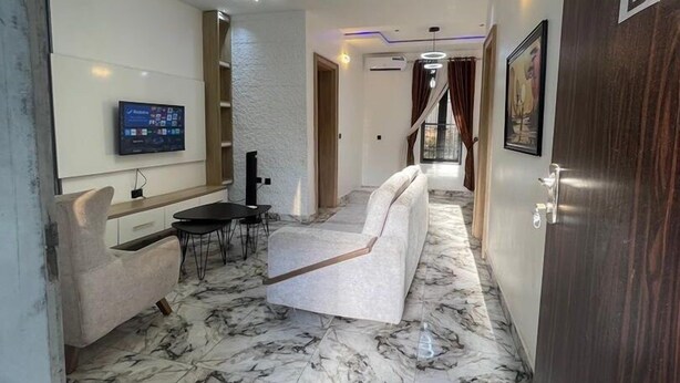 A modern living room with a sofa, a TV mounted on the wall, and a marble floor. - Deroche Apartment (Abuja)