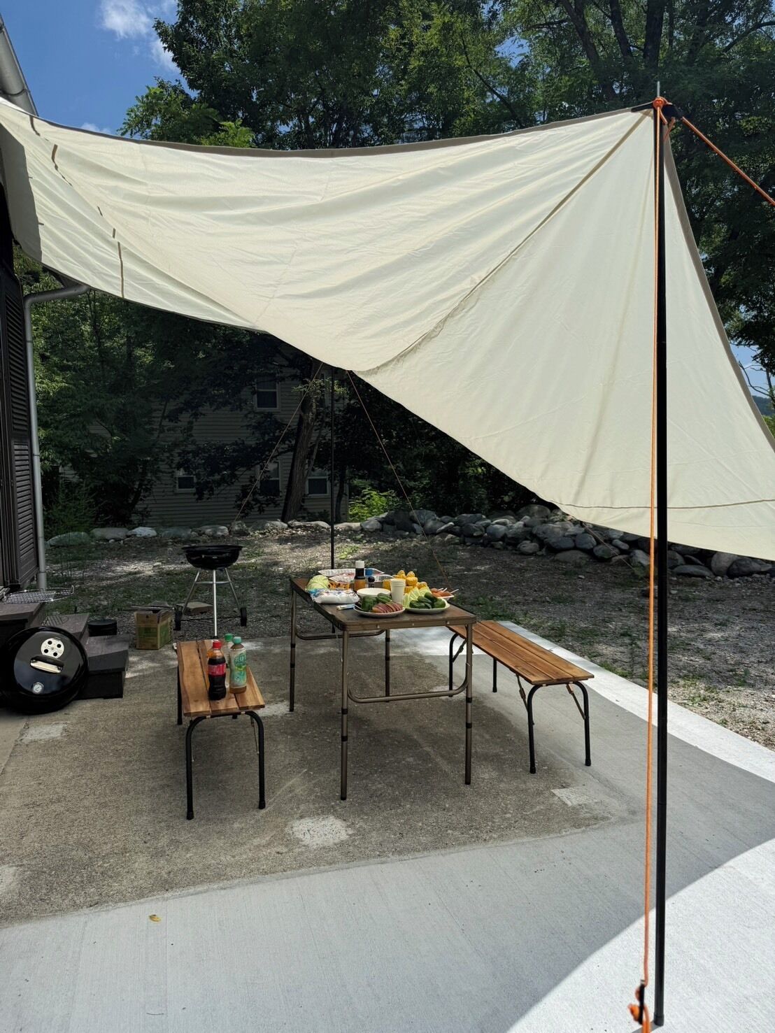 An outdoor dining area with a table and benches, a grill, and a canopy.