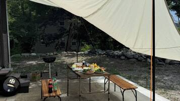 An outdoor dining area with a table and benches, a grill, and a canopy.