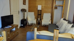 Uma sala de estar com televisão, duas poltronas, um sofá, uma mesa de centro e piso de madeira.