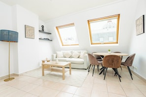 A modern living room with a sofa, coffee table, and dining area with chairs. There are two windows with views of buildings. - Paris chic elegance between Opéra and department stores (Paris)