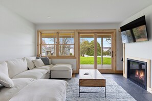 Un salon moderne comprenant un canapé, une table basse, une cheminée et de grandes fenêtres donnant sur un paysage verdoyant.