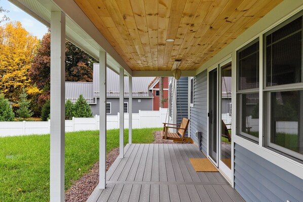 Une véranda abritée avec une chaise suspendue, une terrasse en bois et une vue sur le jardin arrière.