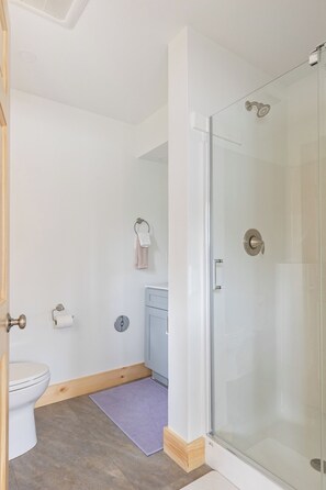 Une salle de bain comprenant des toilettes, une douche avec une porte en verre, un porte-serviettes avec des serviettes et un petit lavabo.