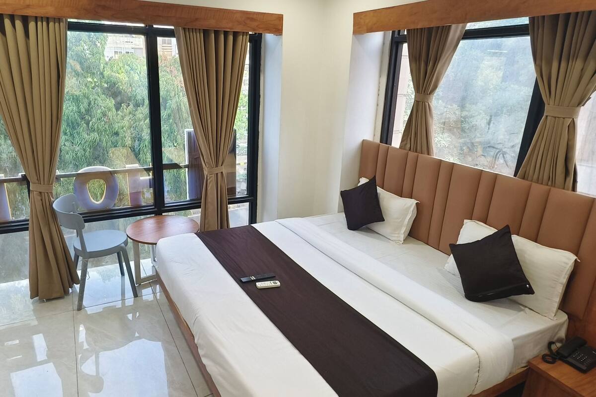 A hotel room with a bed, a desk, a chair, a small table, and a balcony with curtains.