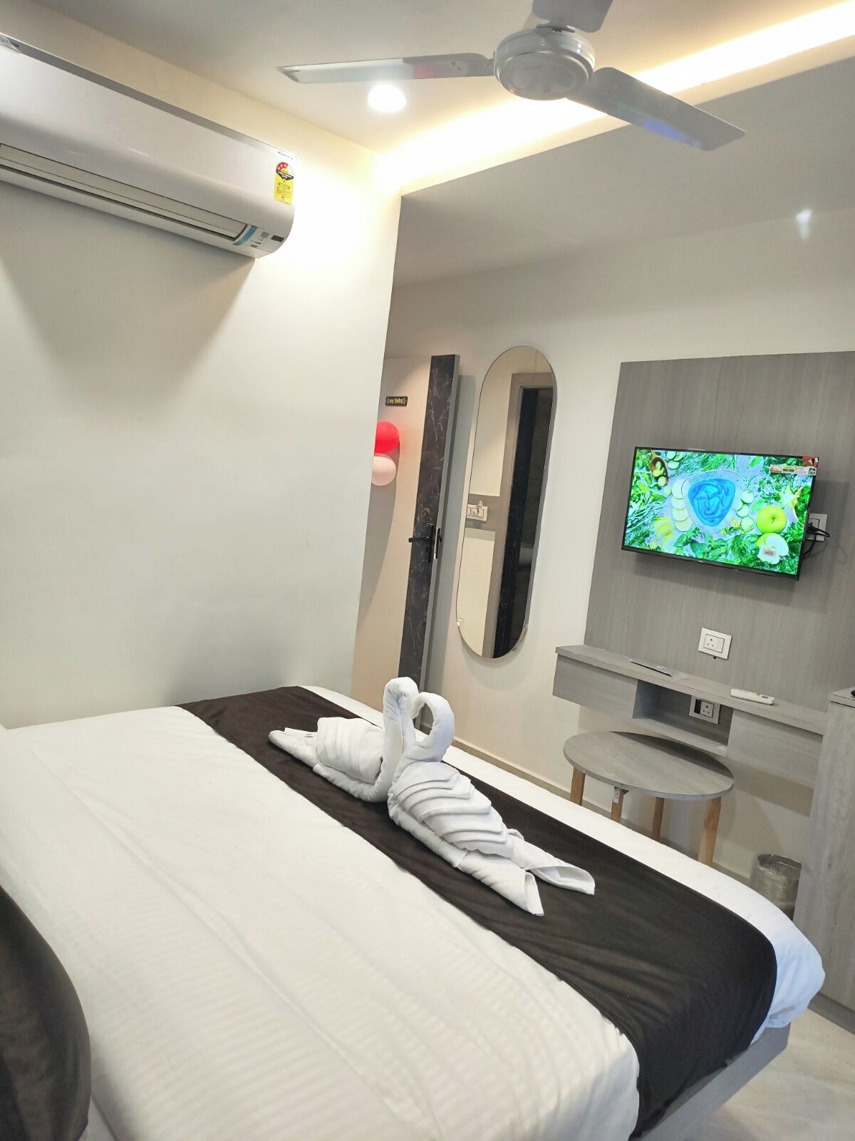 A modern hotel room with a bed, a TV mounted on the wall, and a ceiling fan.