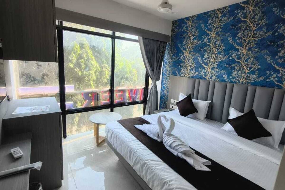 A modern hotel room with a large bed, a desk, and a view of greenery outside.