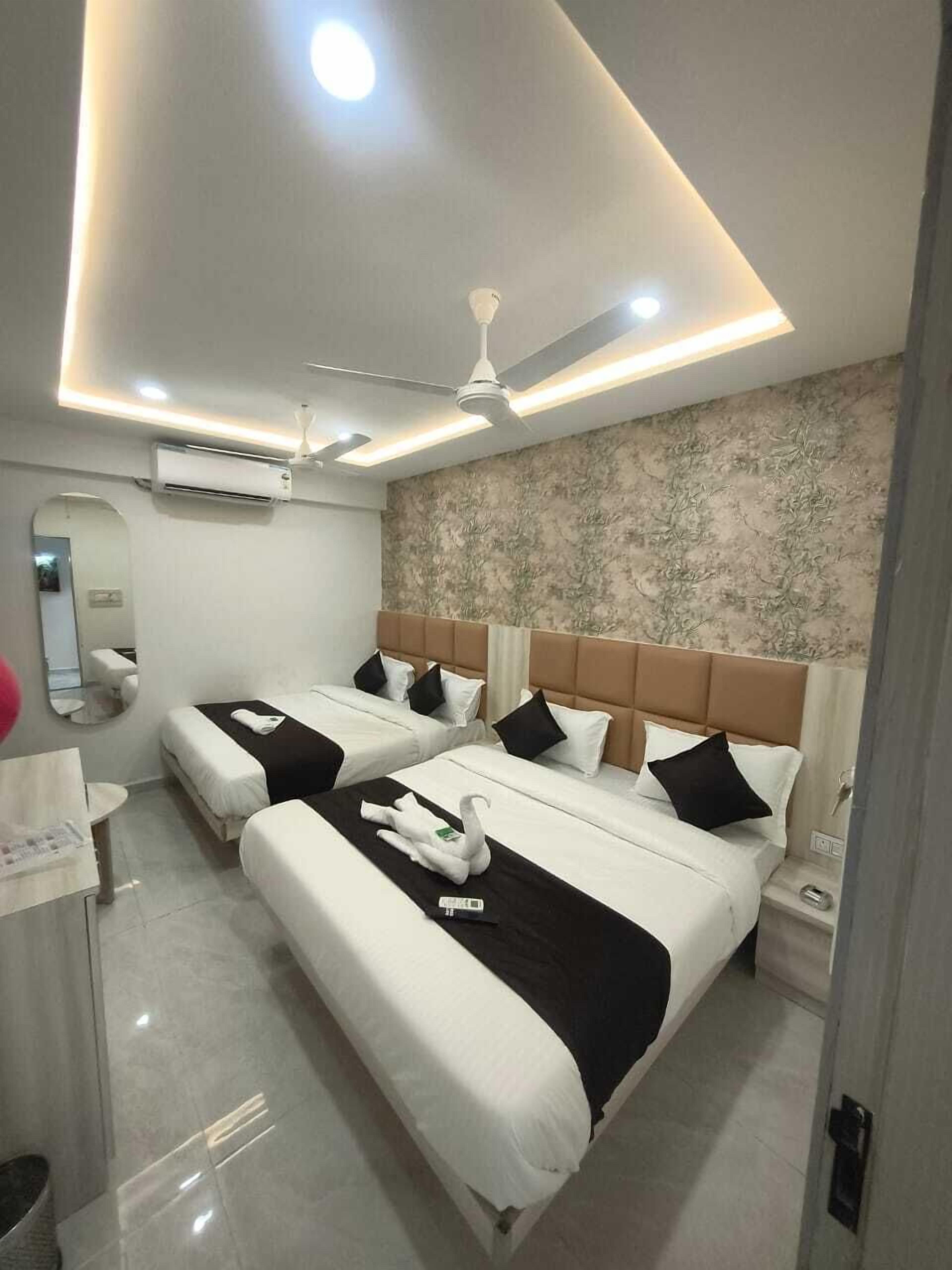 Une chambre d’hôtel avec deux lits, un ventilateur de plafond, des spots encastrés, un appareil de climatisation, un miroir et une salle de bain avec un lavabo et des toilettes.