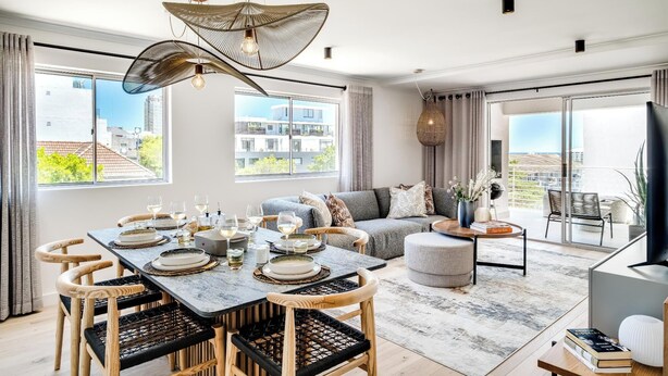 Een moderne woonkamer met een eethoek, grote ramen en een balkon.