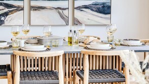 Een eettafel gedekt met witte borden, glazen en flessen, omringd door houten stoelen met geweven zitvlakken.
