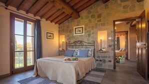 Una camera da letto con parete in pietra, soffitto in legno, un letto con un vassoio per la colazione e vista dalla finestra.