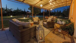 Una terrazza esterna con mobili in vimini, un lampadario e una piscina sullo sfondo.