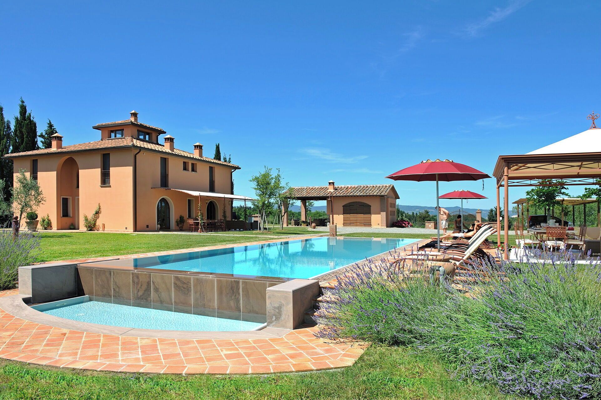 A swimming pool with a patio area, a covered seating area, and a large house with a tiled roof.