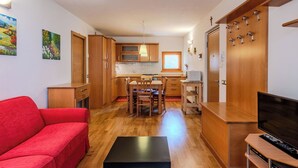 Ett kompakt bostadsutrymme med ett litet kök, en matplats, en röd soffa, ett svart bord och en tv.
