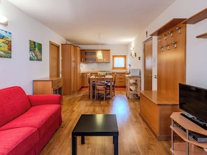 A compact living space with a kitchenette, a dining area, a red sofa, a black table, and a TV. - Cosy apartment for 5 people with TV and panoramic view (Carisolo)