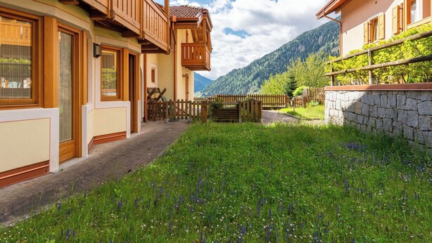 En traditionell chalet med träbalkonger, en stenmur och en gräsbevuxen innergård.