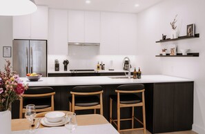 A modern kitchen with a central island, white cabinetry, and a dining area with wooden chairs. - Elevated 2-Bed, 2-Bath Condo with Curated, Editorial-Inspired Interior by Revelstoke Mountain Resort (Revelstoke)