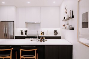 A modern kitchen with white cabinetry, stainless steel appliances, and a central island with bar stools. - Elevated 2-Bed, 2-Bath Condo with Curated, Editorial-Inspired Interior by Revelstoke Mountain Resort (Revelstoke)