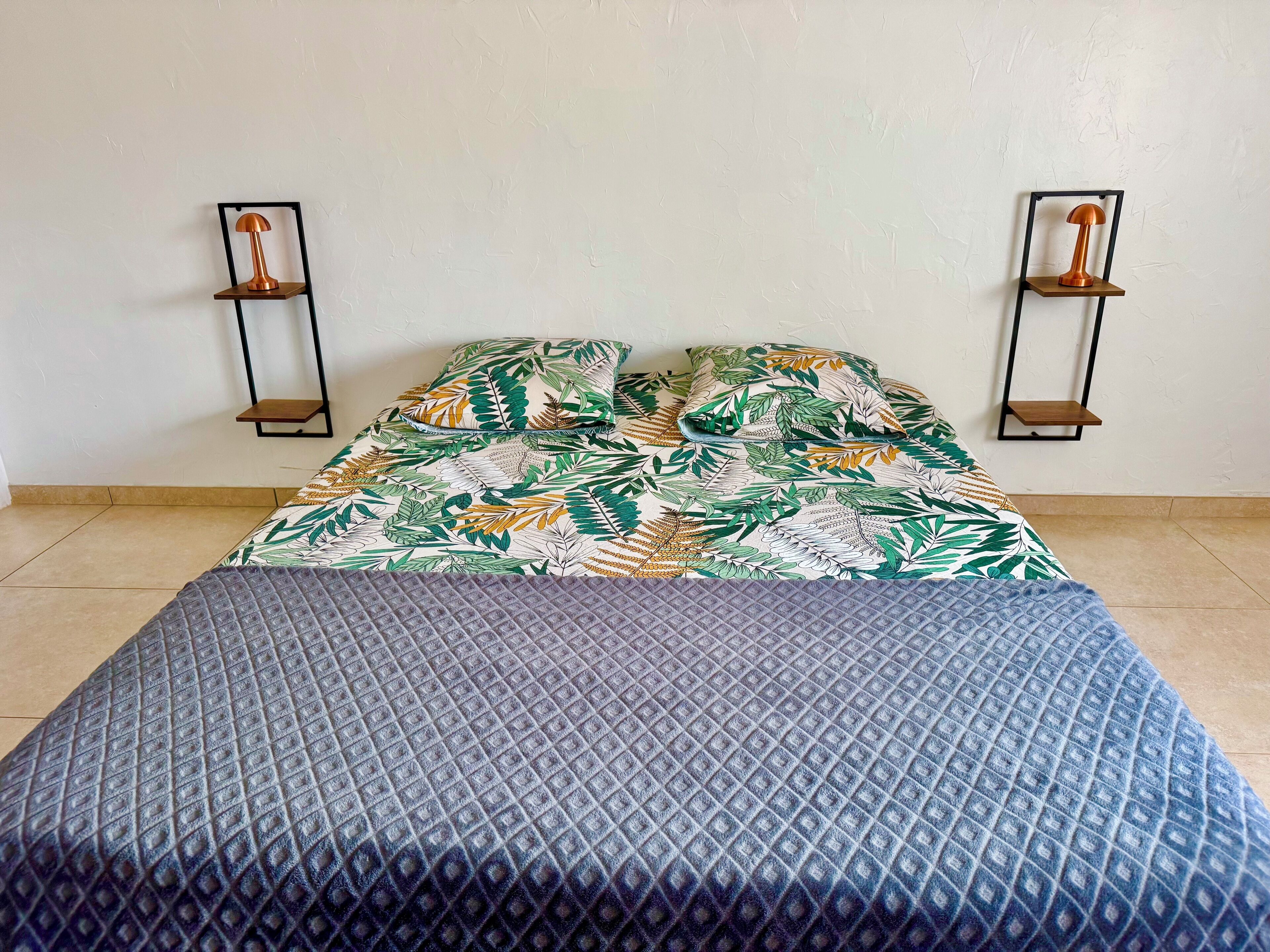 Ein Bett mit floralem Überwurf, einer grauen gesteppten Decke und zwei Wandleuchten.