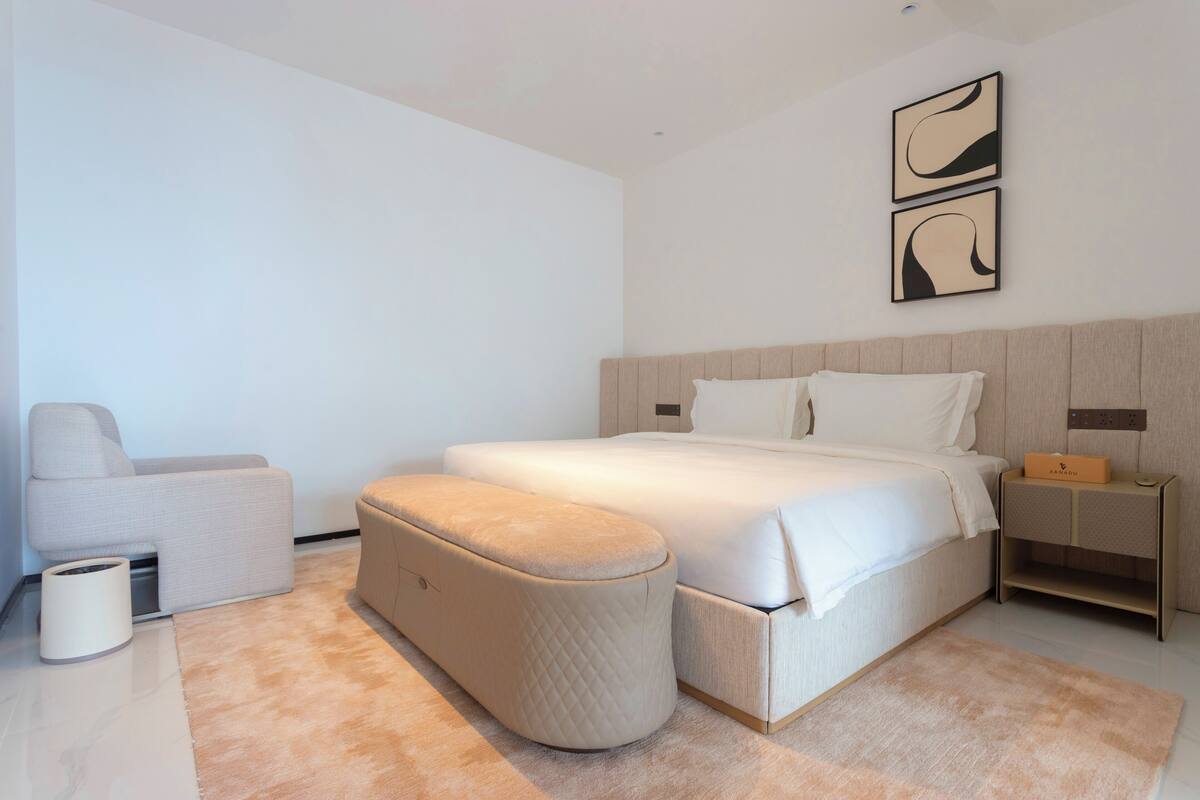 A modern bedroom with a large bed, a bedside table, a chair, and a small table.