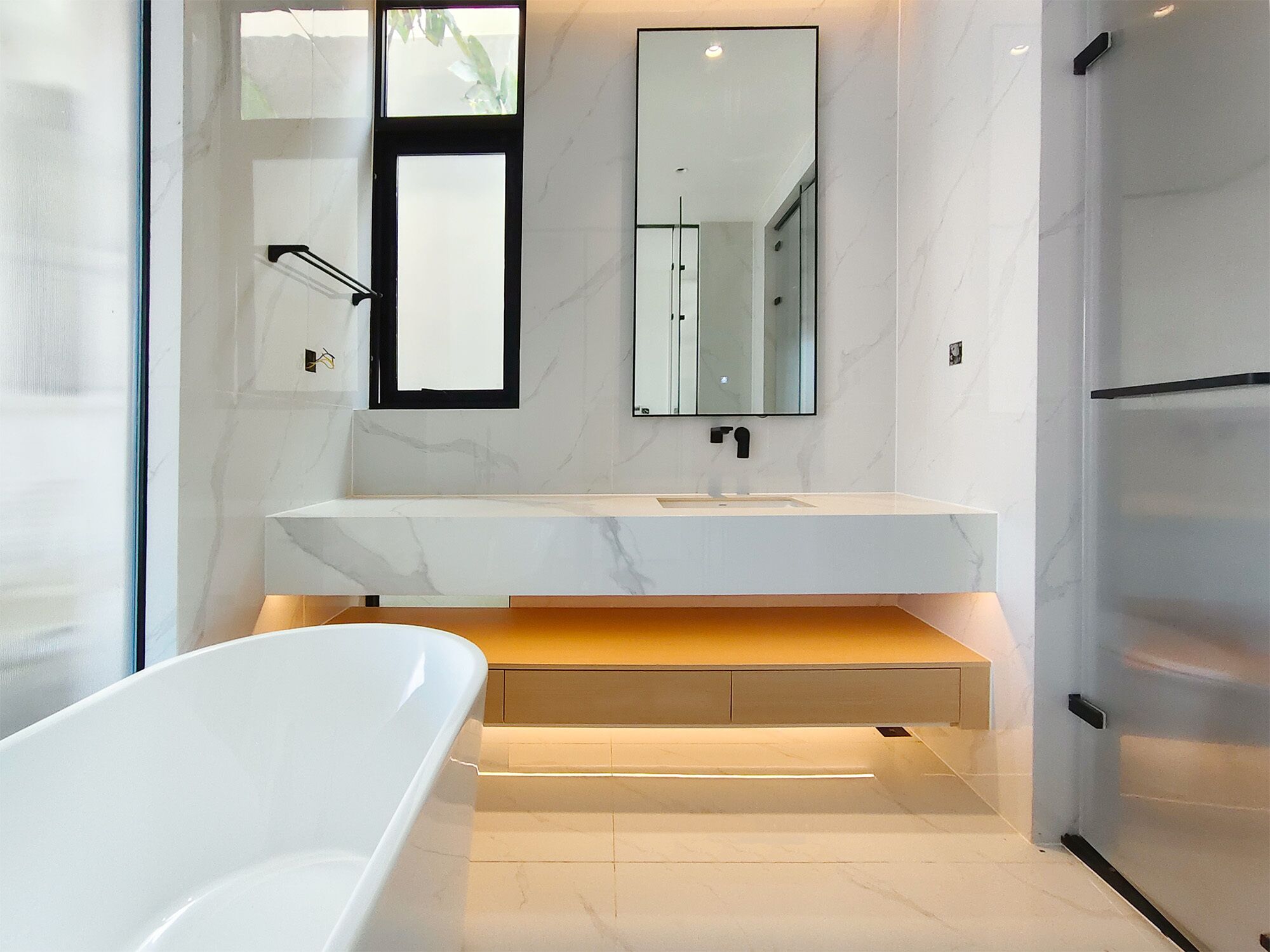 Un baño moderno con una bañera blanca, un espejo grande y una encimera de mármol.