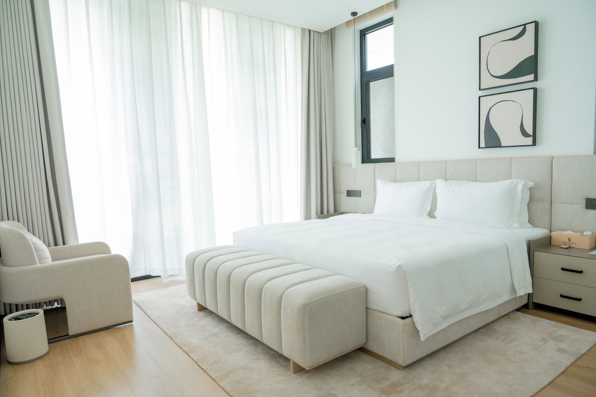 Une chambre d’hôtel moderne avec un grand lit, une table de chevet, une chaise et une fenêtre avec des rideaux.