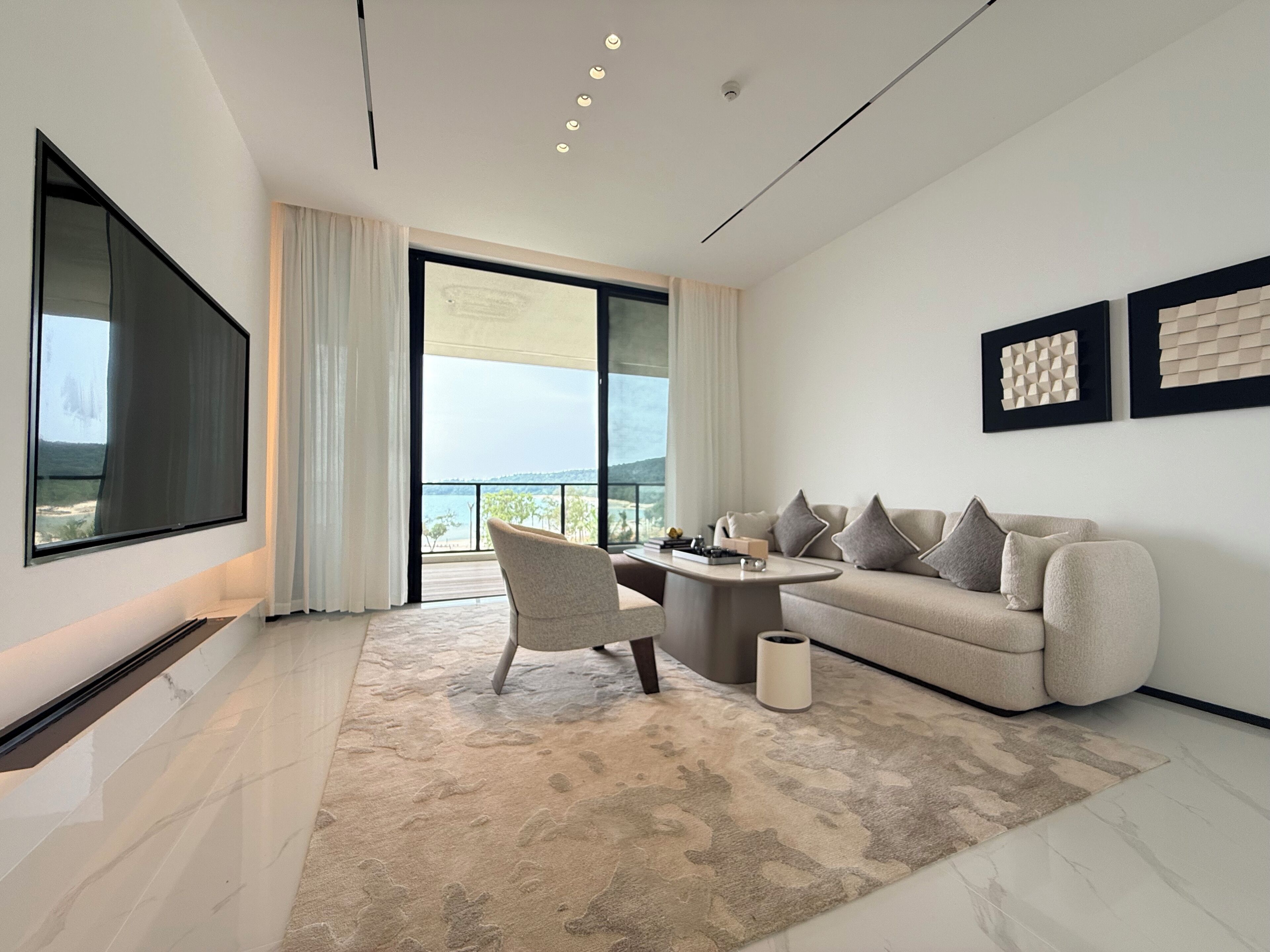 A modern living room with a large TV, a sofa, a coffee table, and a view of the outdoors.