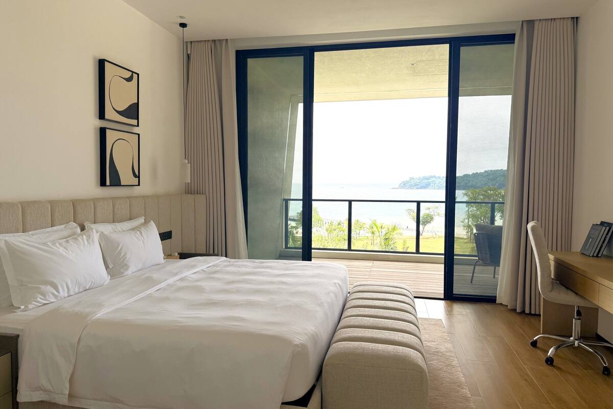A bedroom with a large bed, a desk, and a view of the sea.