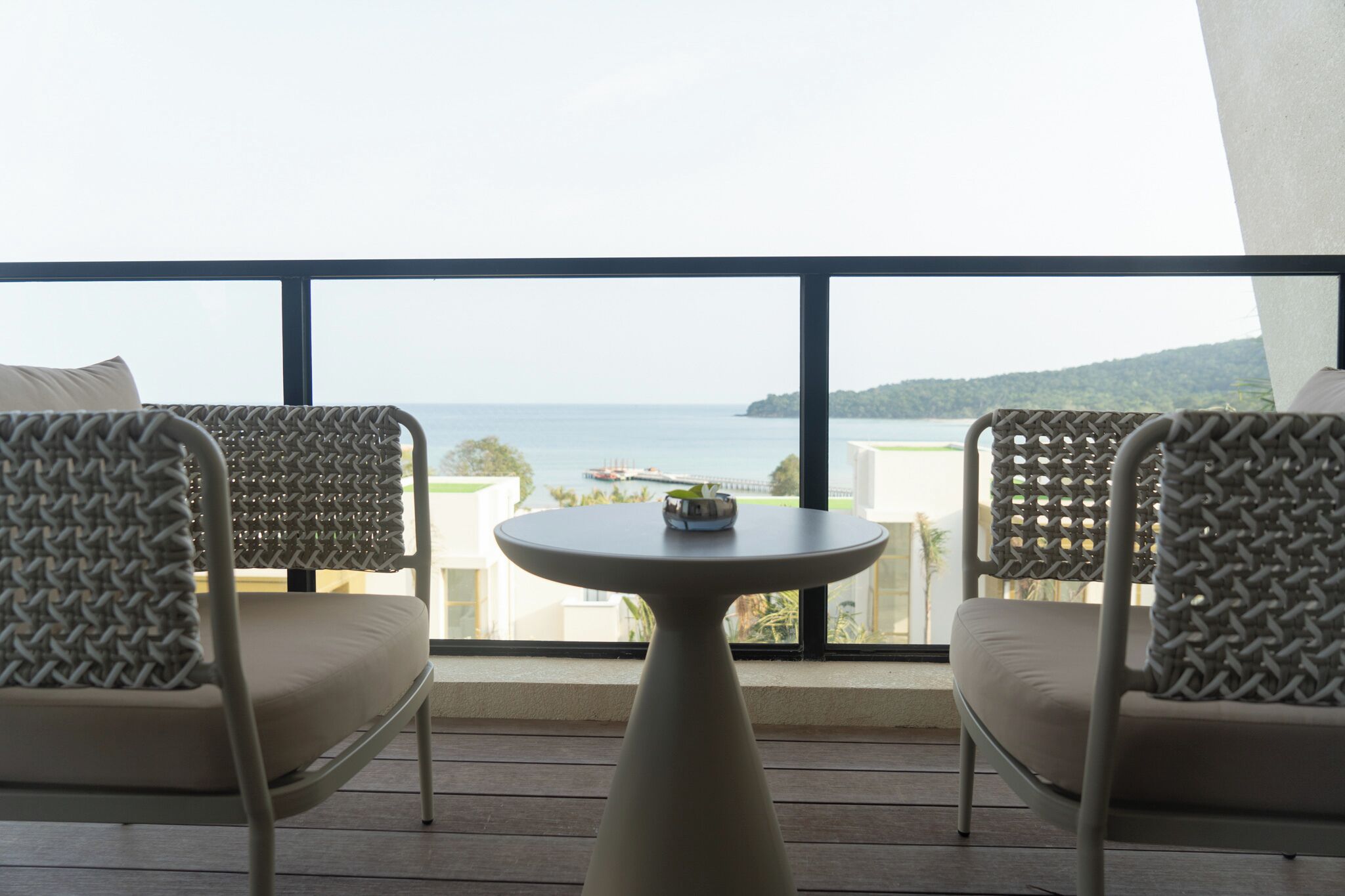 Ein Balkon mit zwei Korbstühlen und einem kleinen runden Tisch, mit Blick auf die Küste.