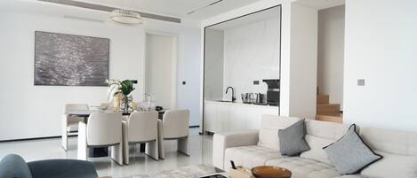 A modern living room with a sofa, coffee table, and a dining area with chairs and a table.