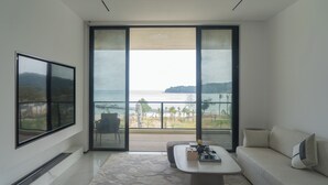 A modern living room with a large sliding glass door leading to a balcony with a view of the sea.