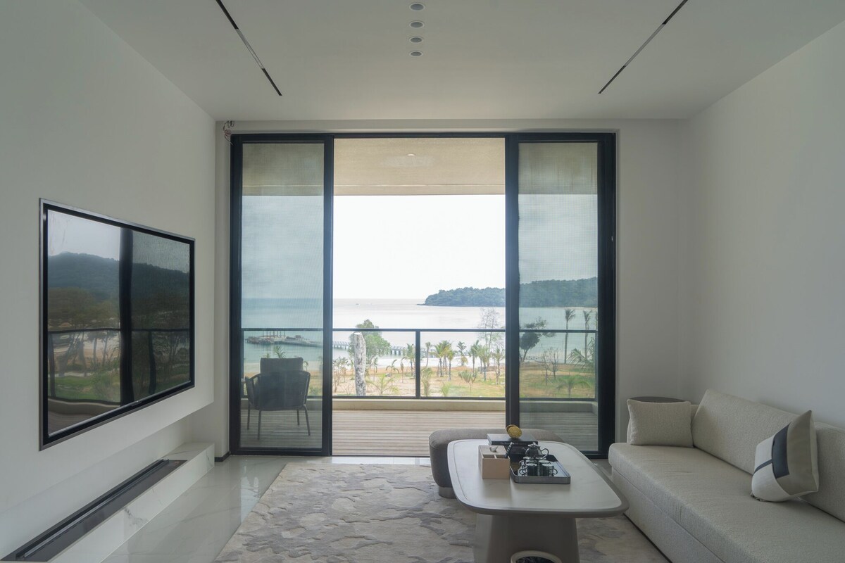 A modern living room with a large sliding glass door leading to a balcony with a view of the sea.