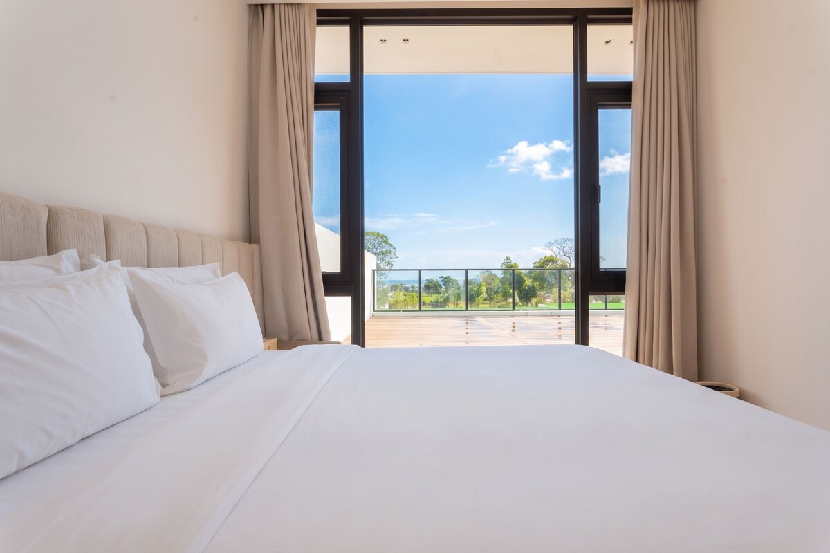 A hotel room with a large bed, a view of the outdoors through a sliding glass door, and a balcony.