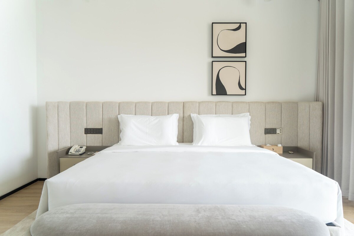 Une chambre d’hôtel moderne avec un grand lit, deux tables de chevet, un téléphone et des œuvres d’art abstraites accrochées au mur.