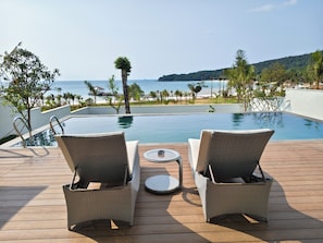 Zona junto a la piscina con dos sillones de mimbre y una pequeña mesa, con vistas a la playa y al océano.