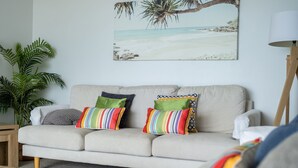 A beige sofa with colorful striped pillows, a large plant, and a beach-themed painting on the wall. - Forster Tower 64 in central Forster. (Forster)