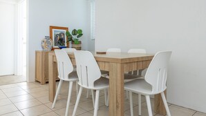 A dining area with a wooden table and white chairs, a small side table with decorative items, and a window with blinds. - Forster Tower 64 in central Forster. (Forster)