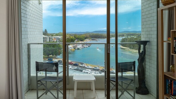 A balcony with a view of a marina, a white chair, and a bookshelf. - Forster Tower 64 in central Forster. (Forster)