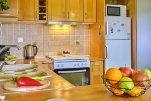 Een keuken met houten kastjes, een fornuis, een magnetron, een koelkast en een schaal met fruit.