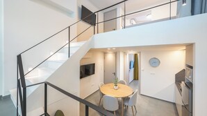 A modern interior with a staircase, a dining area with a round table and chairs, a kitchen with a stove, and a flat-screen TV mounted on the wall. - Athens Secluded Apartment A, Athens Secluded Apartments (Athens)