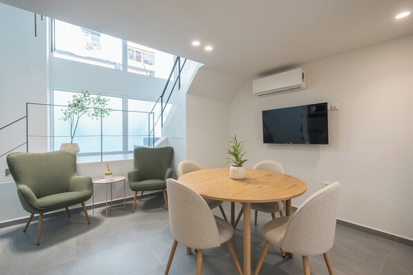 Une salle de réunion moderne, dotée d’une table ronde en bois, de quatre chaises, d’une plante en pot et d’un téléviseur à écran plat fixé au mur.