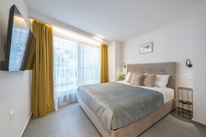 Une chambre à coucher moderne avec un grand lit, un téléviseur fixé au mur et une table de chevet avec une lampe.
