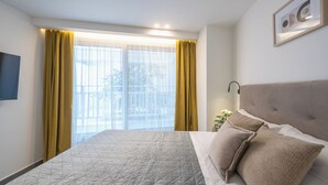 A modern hotel room with a large bed, a flat-screen TV, and a balcony with yellow curtains. - Athens Secluded Apartment A, Athens Secluded Apartments (Athens)