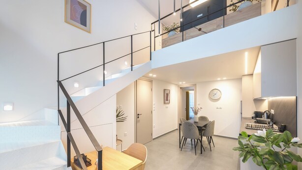Interior moderno com escada que leva a um segundo andar, área de jantar com mesa e cadeiras, e cozinha equipada.
