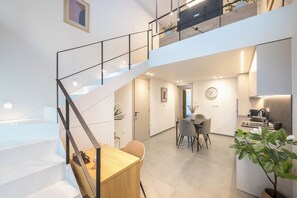 Un intérieur moderne avec un escalier menant à un deuxième étage, un coin repas avec une table et des chaises, et un espace cuisine équipé d’appareils électroménagers.