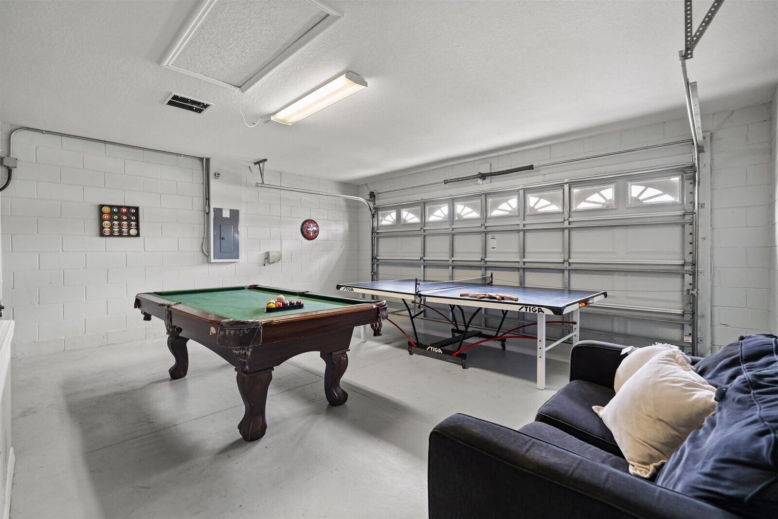 A room with a pool table, a ping pong table, a sofa, and a brick wall.