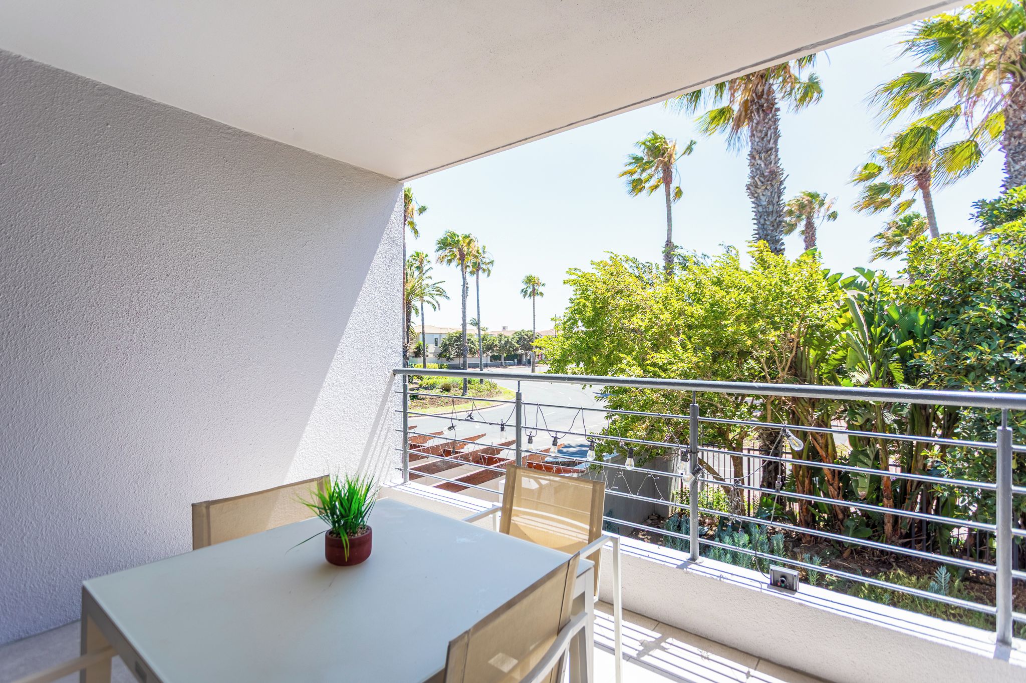 A balcony with a table, chairs, and a potted plant.