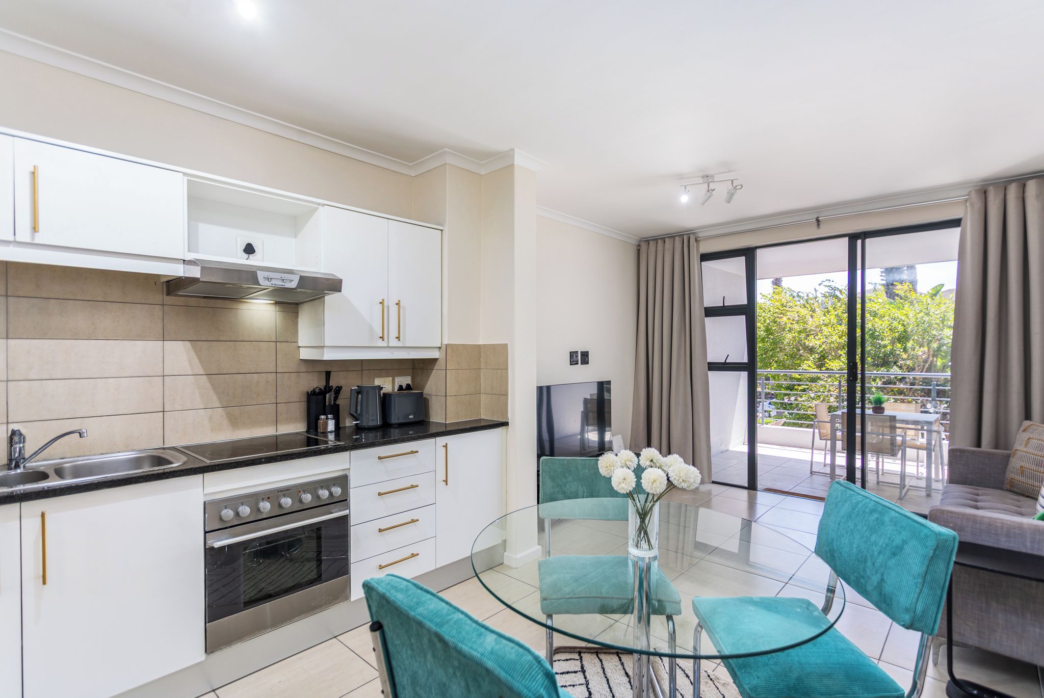 A modern kitchen with white cabinets, a stove, and a dining area with a glass table and teal chairs.