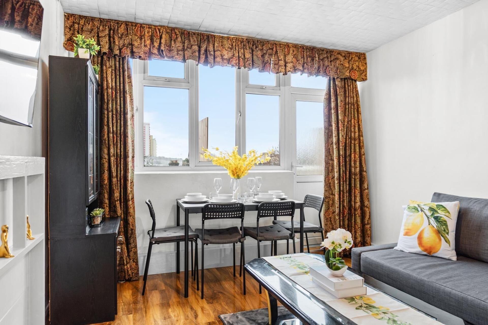 A dining area with a table set for four, a sofa, and a window with curtains.